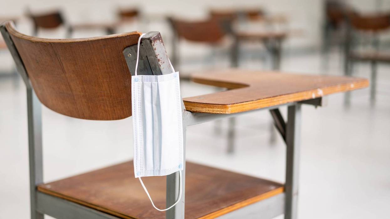 File photo of a medical style face mask hanging off of a student desk in a classroom.