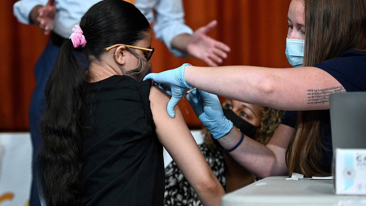 File photo: With New York City Mayor Bill de Blasio (orange tie) and New York City Schools Chancellor Meisha Porter (black mask) looking on, Giret Madina, 14, receives her first dose of the Pfizer BioNTech COVID-19 vaccine at a pop-up vaccine site located at the Lehman High School Campus in the Bronx on July 27, 2021