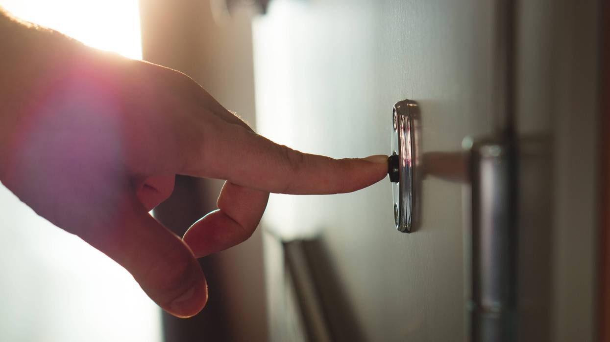 Finger pressing doorbell in sunny apartment building corridor. Close up of male hand ringing door bell in a block of flats. Salesman, fundraiser, guest or visitor behind door. - stock photo