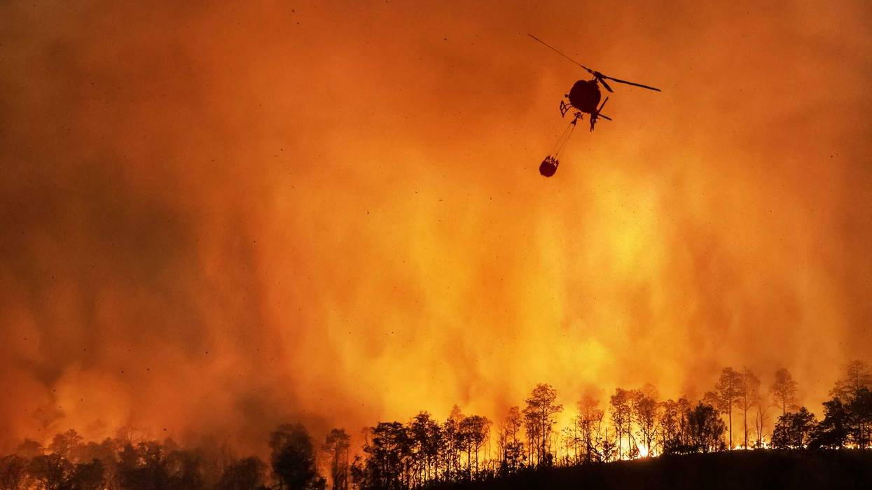 Fire fighting helicopter dropping water over wildfire.