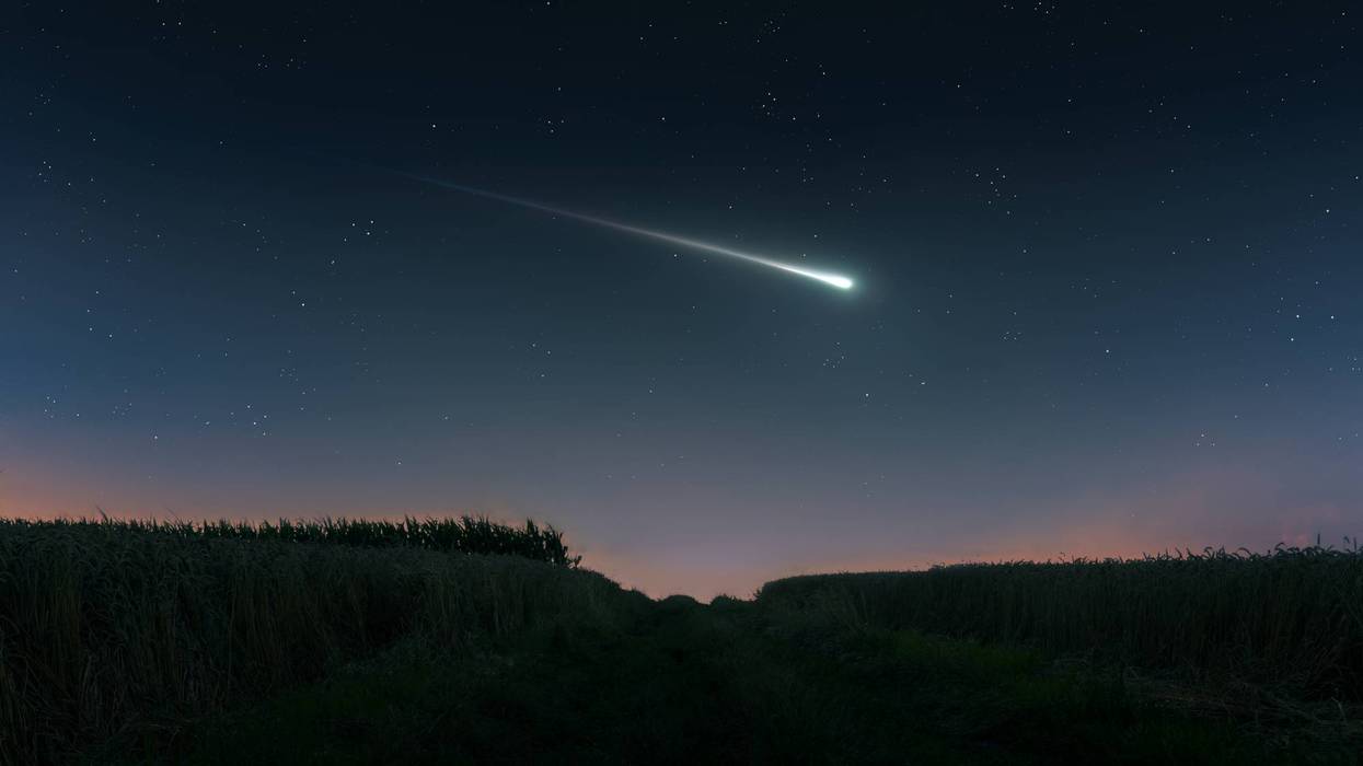Fireball in the evening sky over the fields. Bright shooting star.