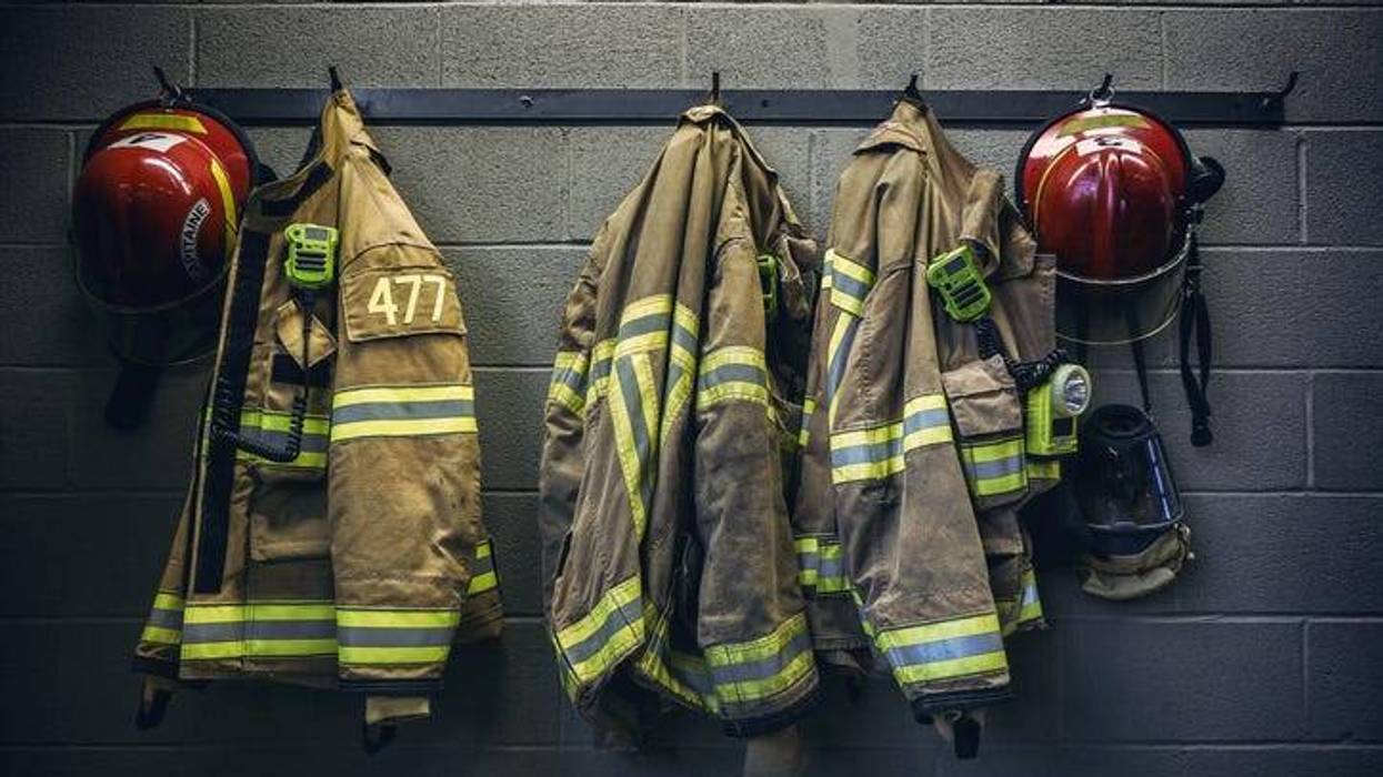 Firefighter uniforms -- coats and helmets -- hanging on a wall in a firehouse.