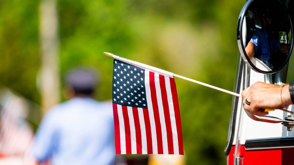 Firefighter waves an American flag from the window of a firetruck during a patriotic US parade for Memorial Day, Flag Day, or July 4th