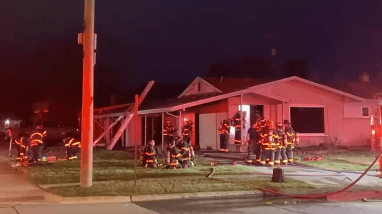 Firefighters at night, responding to a house fire with emergency lights reflecting.