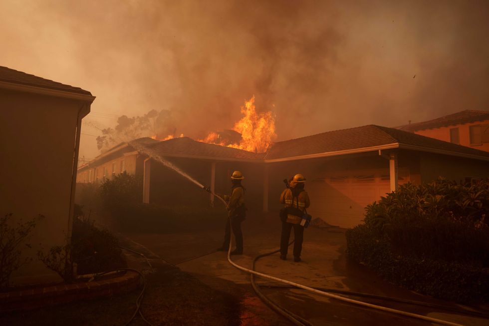 Firefighters spray a home burning during the Palisades Fire on January 8, 2025 in the Pacific Palisades neighborhood of Los Angeles, California. Multiple wildfires fueled by intense Santa Ana Winds are burning across Los Angeles County. Five people have been killed, over 25,000 acres have burned, and 30,000 people have been evacuated.
