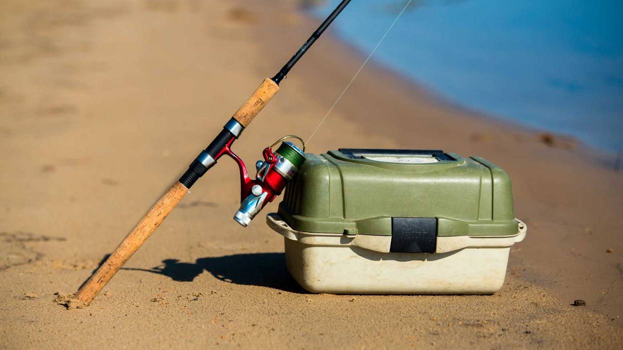 Fishing pole and tackle box on a river shore.