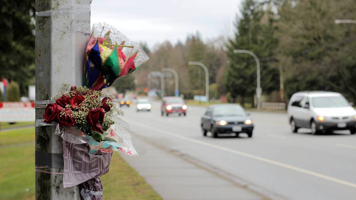 flowers taped up on a street light on the side of a busy road indicating someone's death