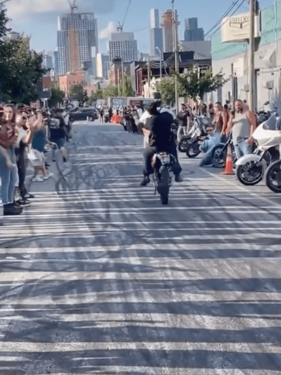 Footage of NYPD Officer Scott on the back of a dirtbike as its operator pops a wheelie.