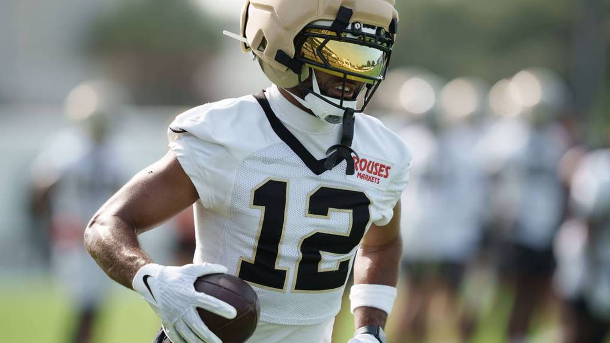 Football player #12 in white jersey, tan helmet with gold visor, holding a football at practice.