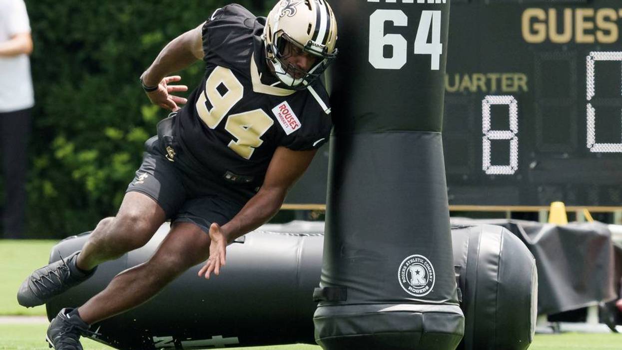Football player #94 in black and gold Saints uniform pushes a training dummy at practice.
