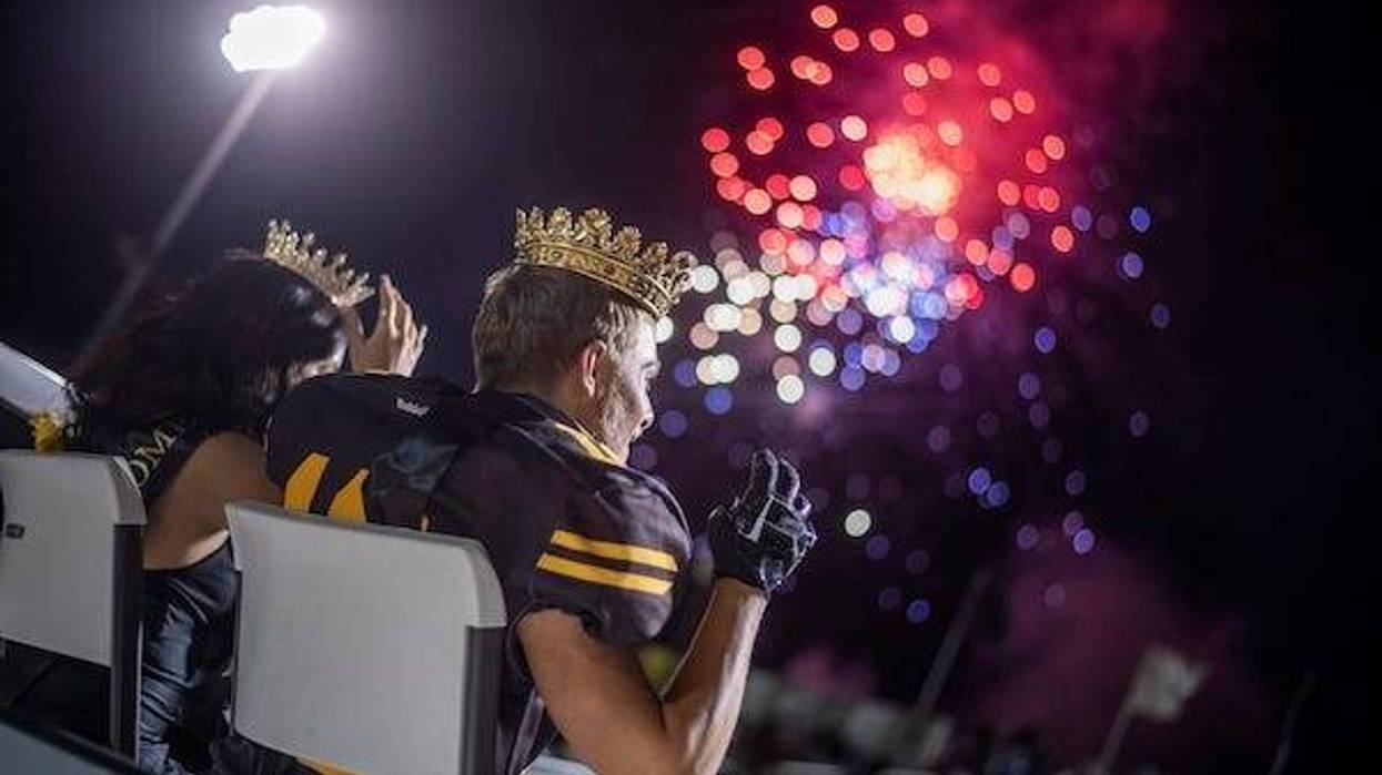 Football player and cheerleader crowned homecoming king and queen against fireworks