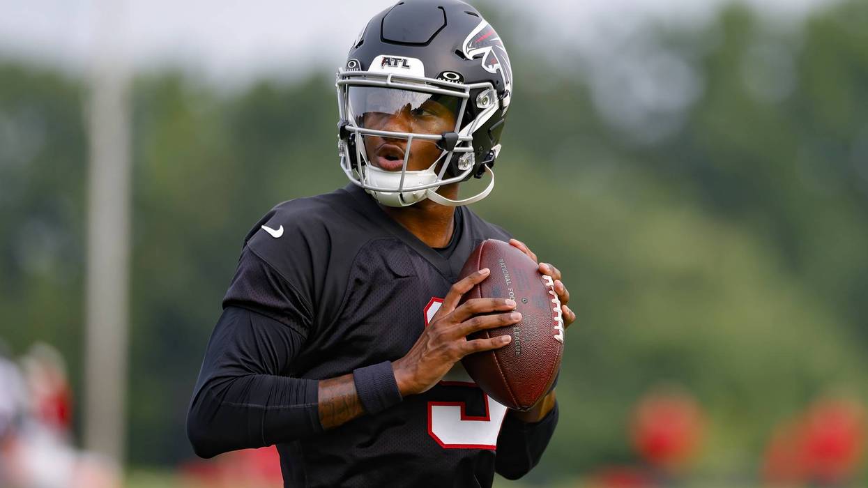 Football player in black Atlanta Falcons helmet and jersey holds a football.