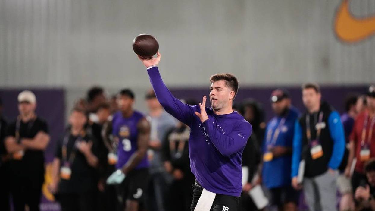 Football player in purple #18 shirt throws a football indoors with arm raised.