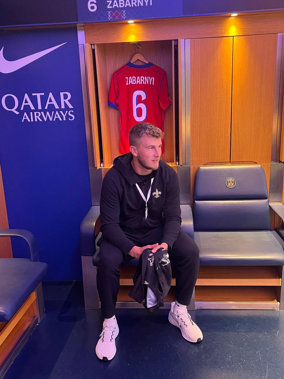 Footballer Zabarnyi sits in a modern locker room; his #6 jersey hangs behind him. Nike, Qatar Airways, PSG logos visible.