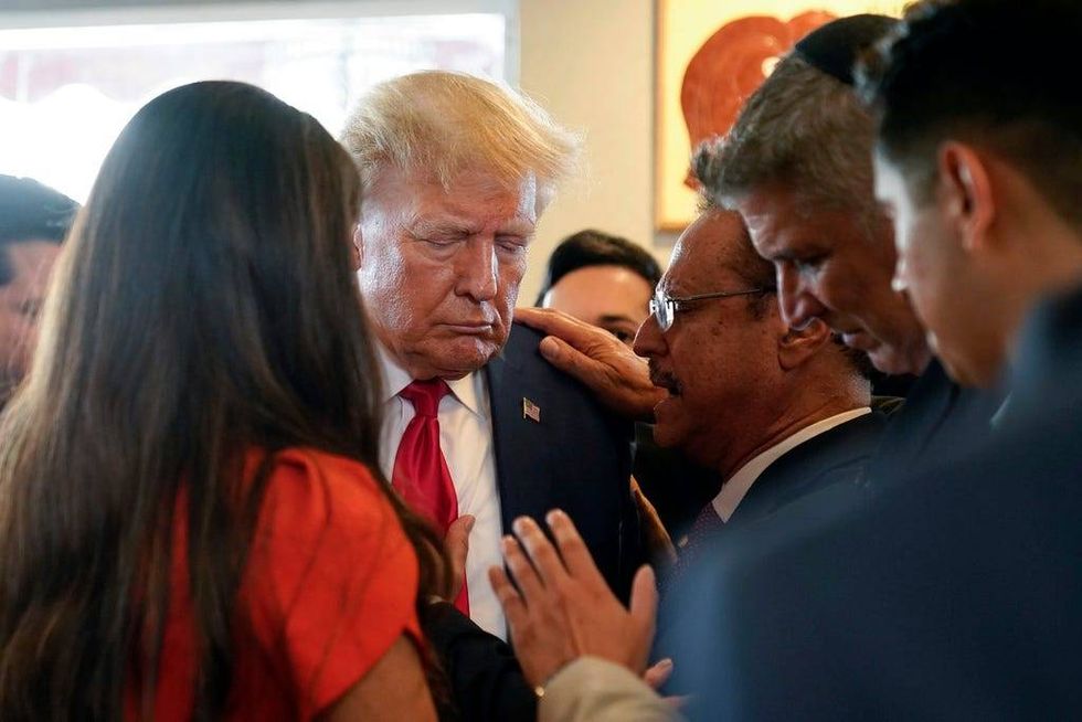 Former President Donald Trump prays with pastor Mario Bramnick, third from right, and others at Versailles restaurant on Tuesday, June 13, 2023, in Miami. Trump appeared in federal court Tuesday on dozens of felony charges accusing him of illegally hoarding classified documents and thwarting the Justice Department
