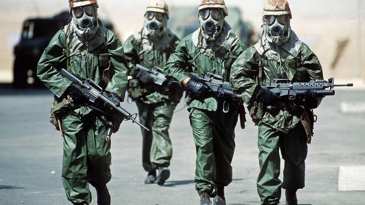Four soldiers from the 82nd Airborne Division walk around their camp wearing rain suits, gloves and M-17A1 protective masks as they try to acclimate their bodies to the heat of the Saudi summer during Operation Desert Shield.