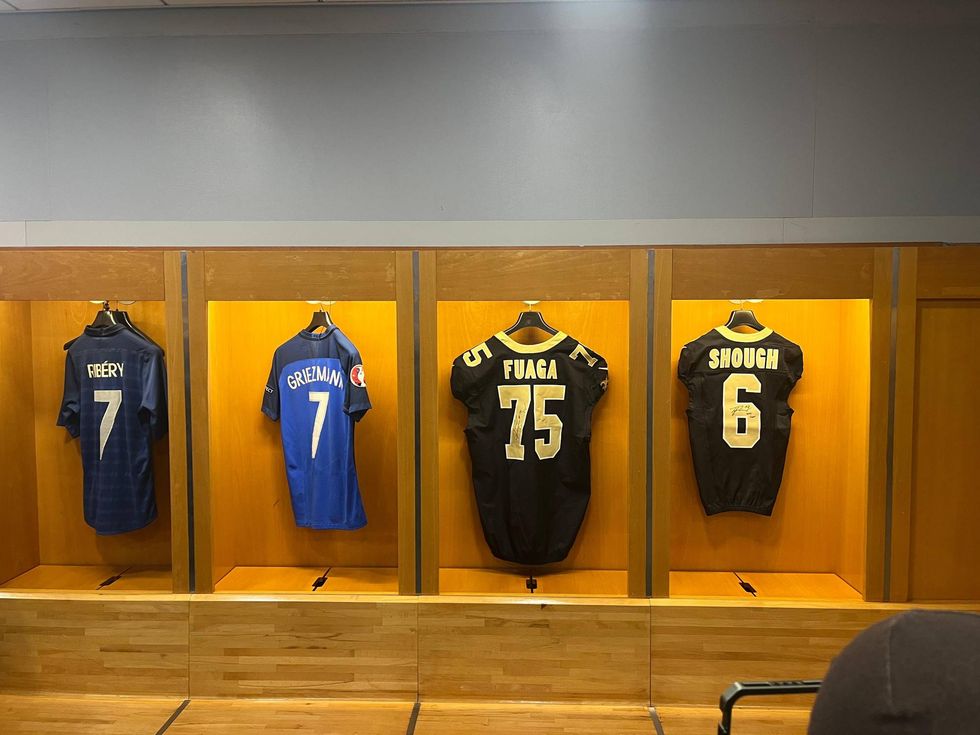 Four sports jerseys in wooden lockers: Rib\u00e9ry 7, Griezmann 7 (soccer); Fuaga 75, Shough 6 (football).