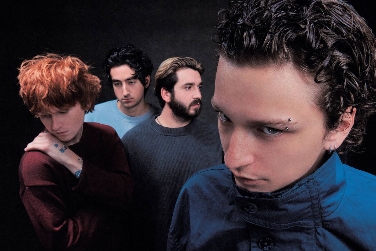 Four young men in a band. One with eyebrow piercing stares, another with red hair looks down.