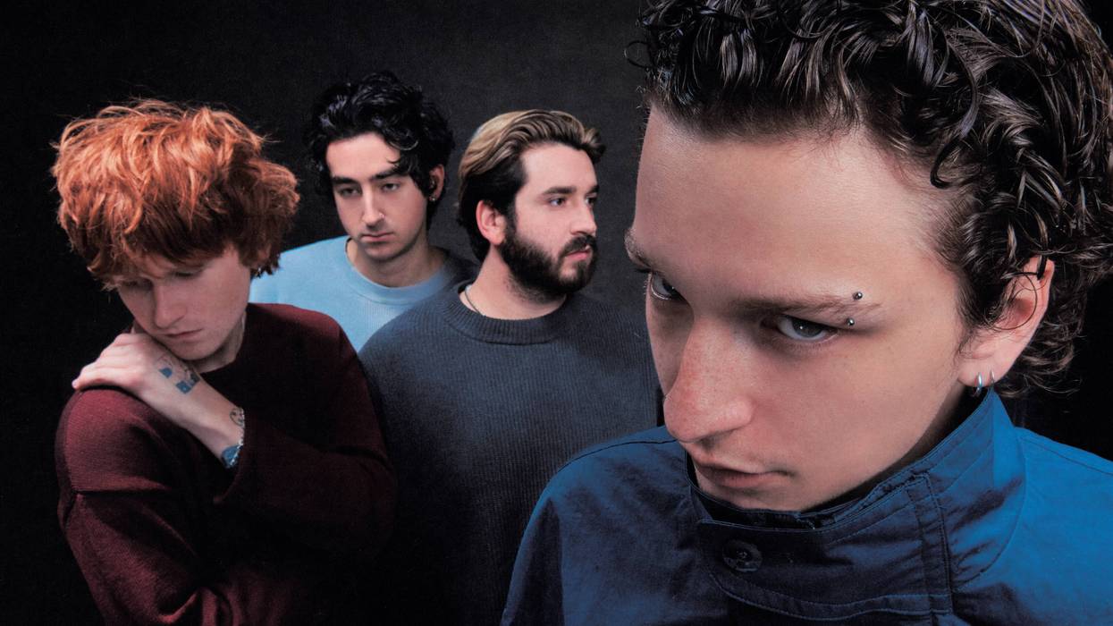 Four young men in a band. One with eyebrow piercing stares, another with red hair looks down.