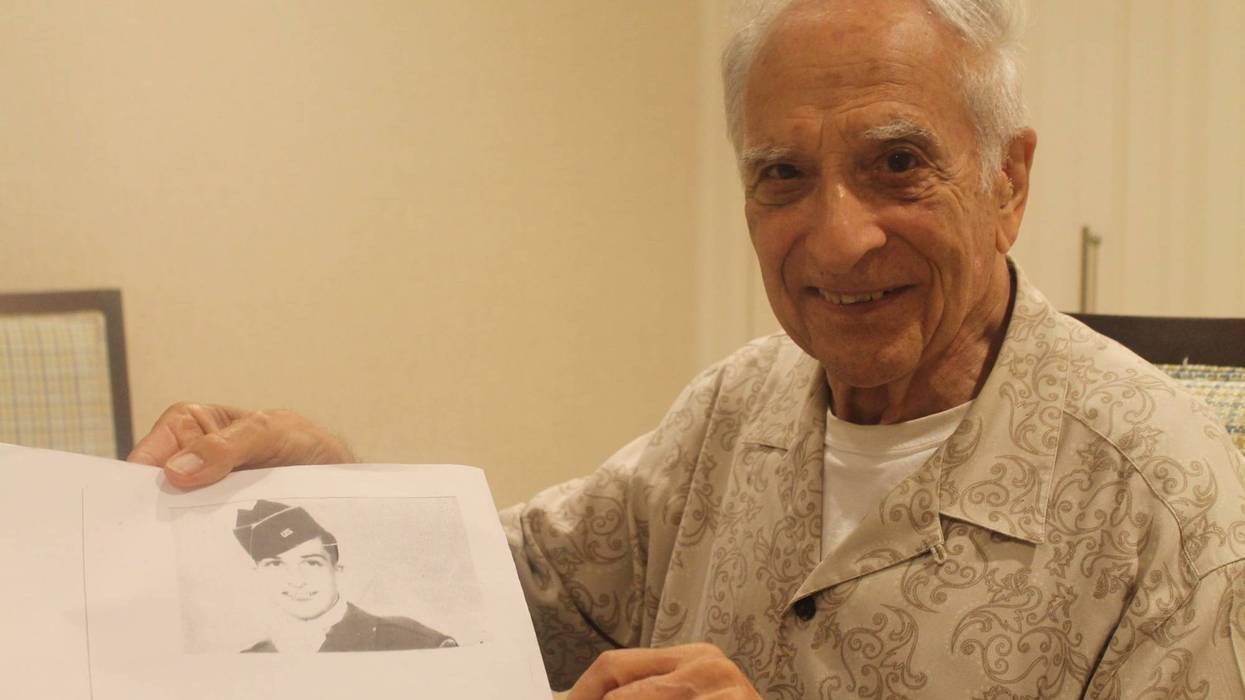 Frank Cohn holding a picture of himself in uniform during World War II.