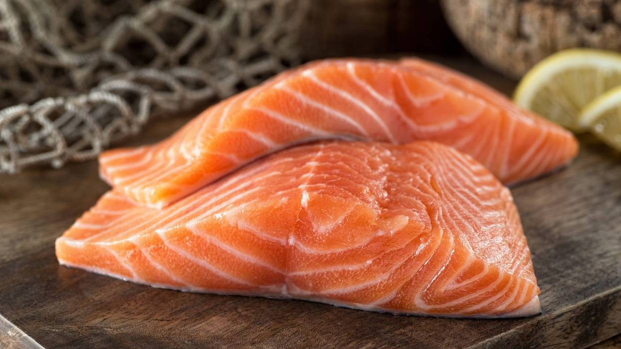 Fresh raw salmon fillets on a wooden board with lemon and fish net background.