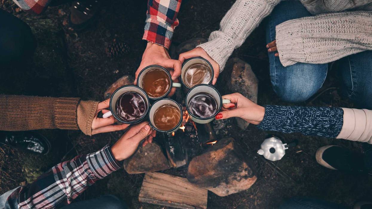 Friends toasting each other while warming up near the campfire