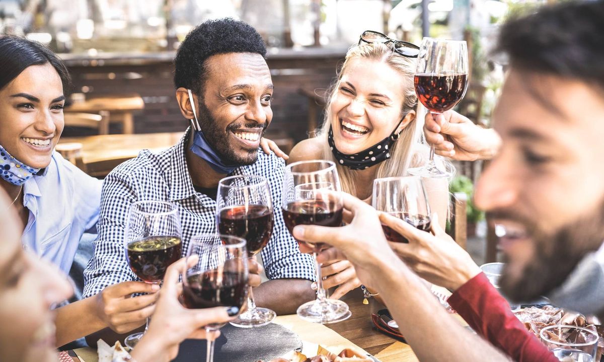 Friends toasting red wine at outdoor restaurant bar with open face mask