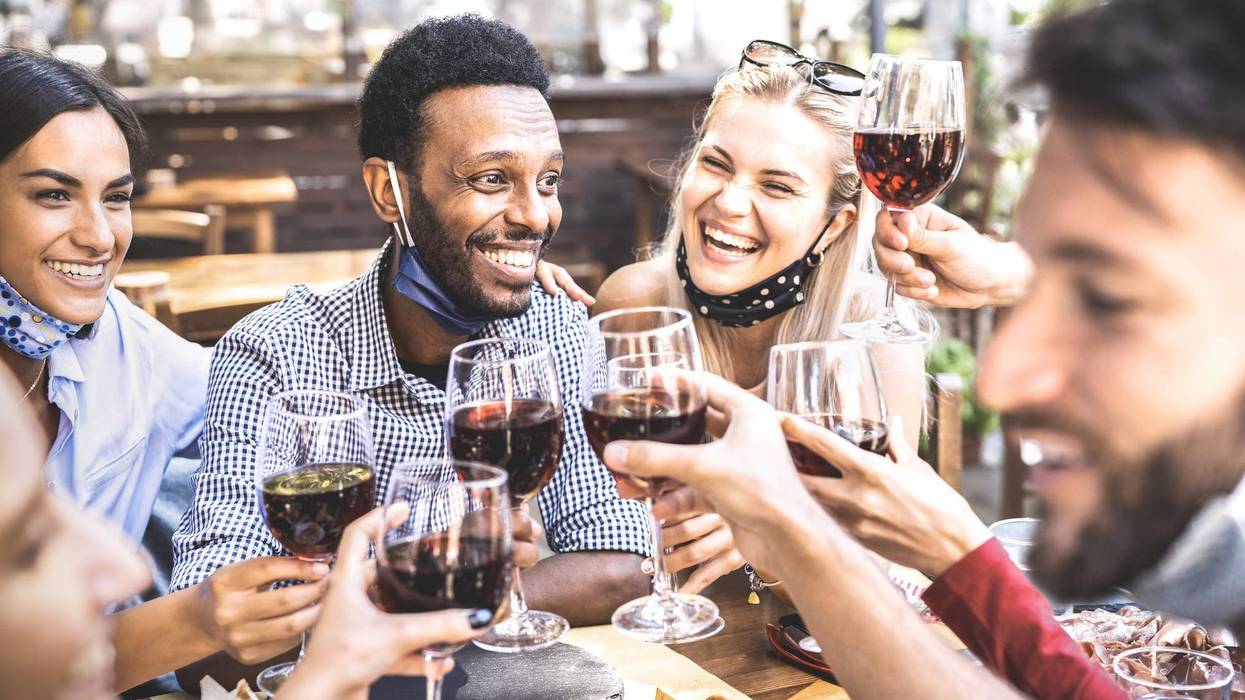 Friends toasting red wine at outdoor restaurant bar with open face mask