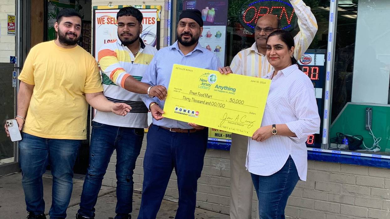 From left: Two employees, Tony Singh, Harish Patel and Raj Singh hold up a check their store received for selling a $221 million winning Powerball jackpot ticket, June 11, 2024.