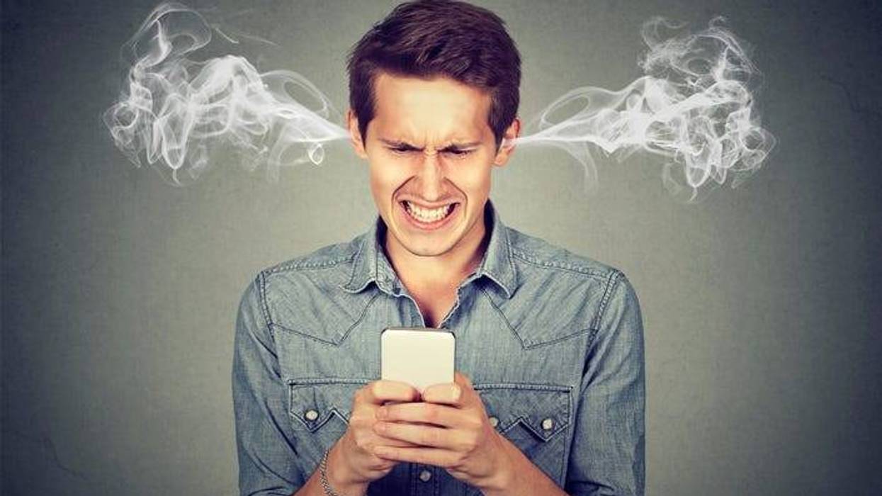 Frustrated angry man reading a text message on his smartphone blowing steam coming out of ears