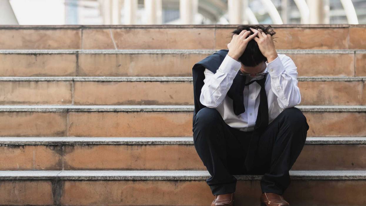Frustrated man with his head in his hands, sitting on steps.