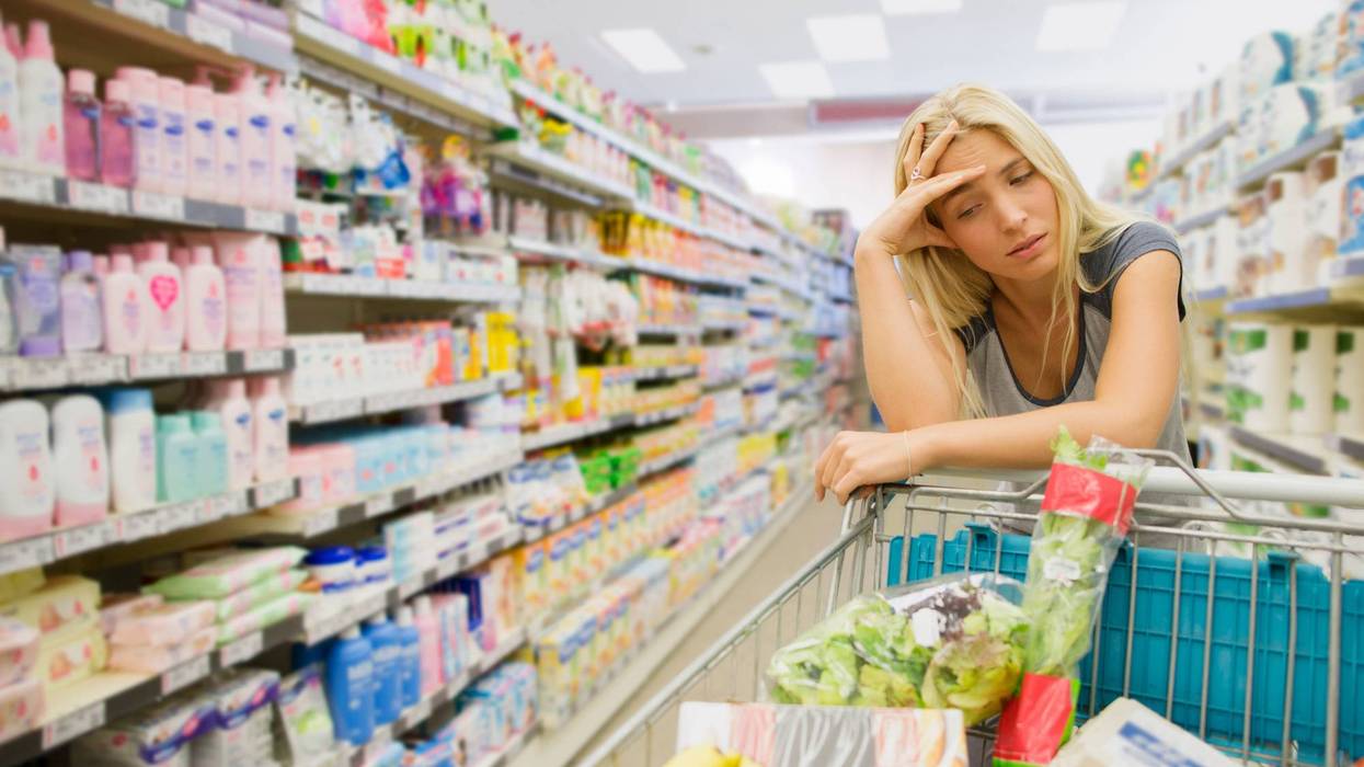 Frustrated woman pushing shopping cart in grocery store - stock photo
