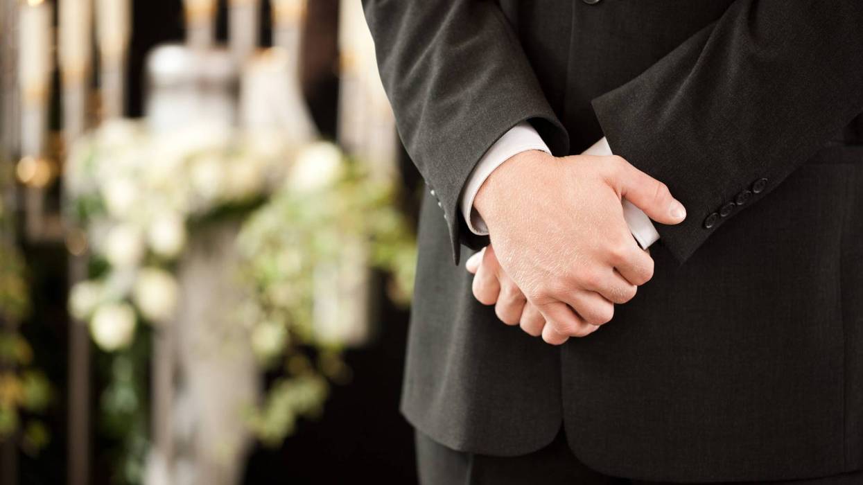 Funeral director stands at a service, an urn surrounded by flowers in the background
