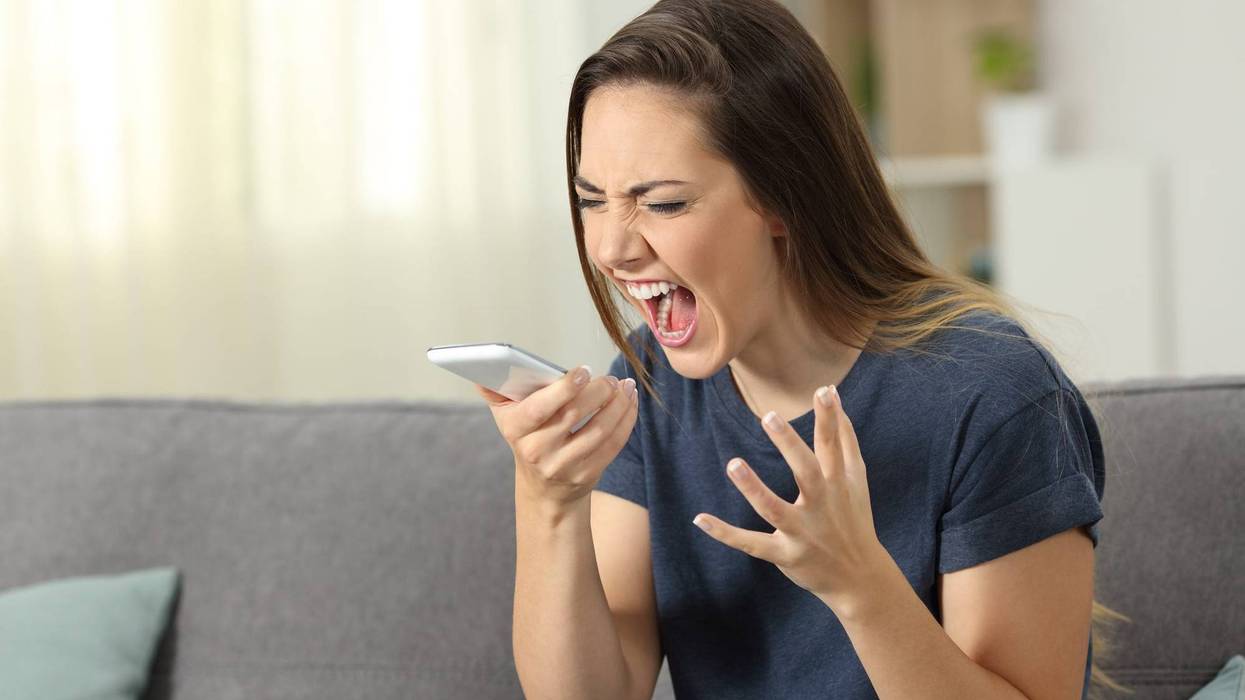 Furious woman shouting to smart phone sitting on a couch in the living room at home