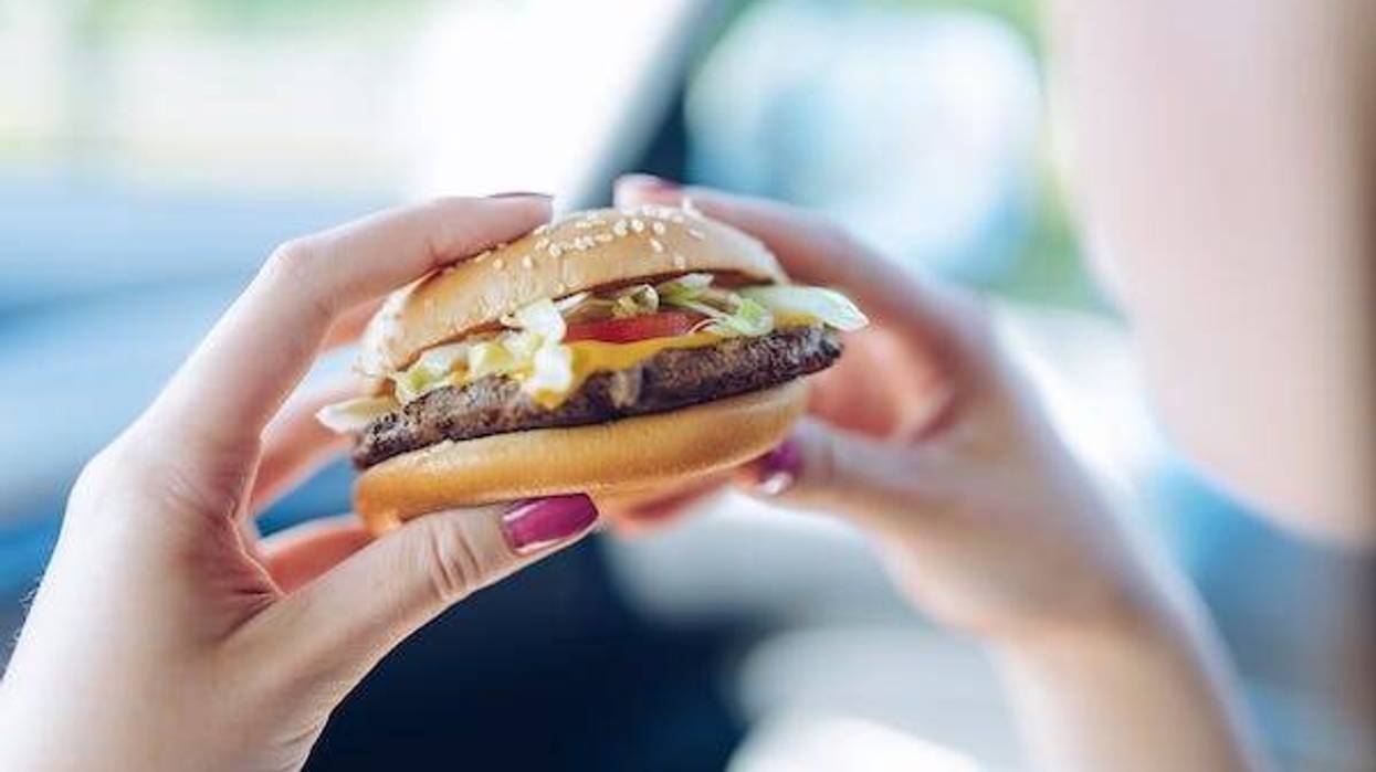 Girl holding a hamburger in her hands sitting in a car.