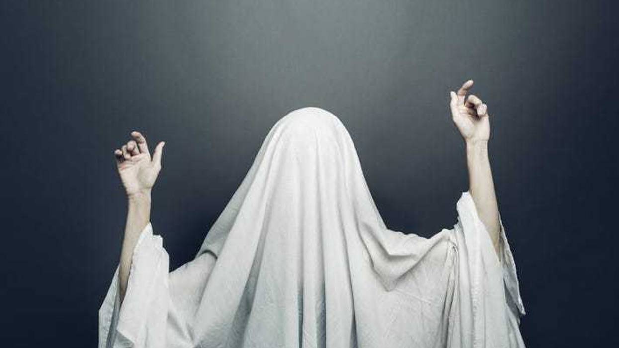 Girl in costume Spooky white ghost with black eyes on a gray background. Halloween minimal concept