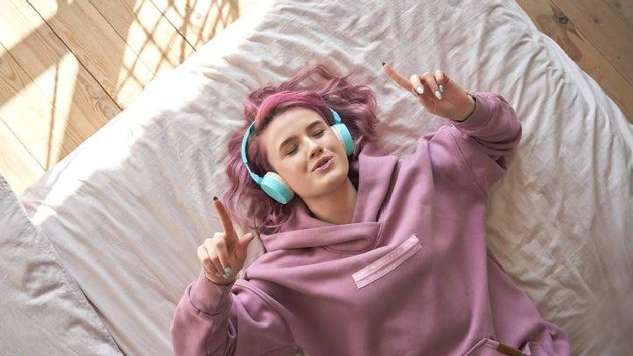 Girl listening to music on headphones on a bed