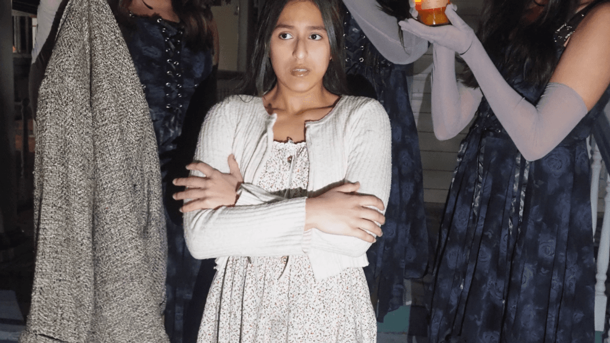 Girl playing Eurydice stands in the cold surrounded by the Fates