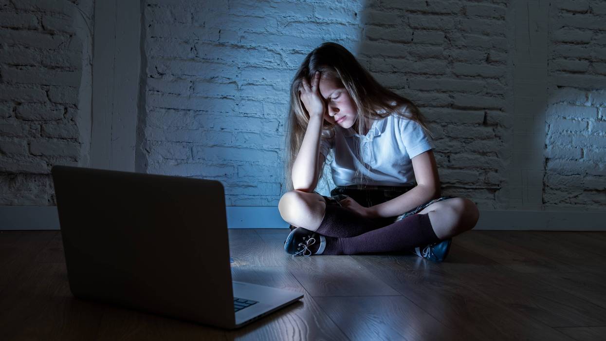 Girl sitting sadly against a wall after getting bullied online