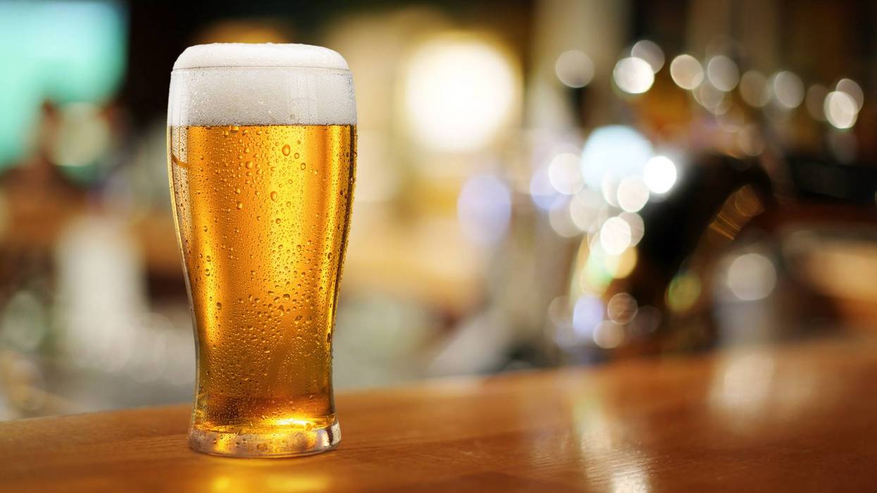 Glass of chilled beer on wooden bar table top and blurred bar interior at the background.
