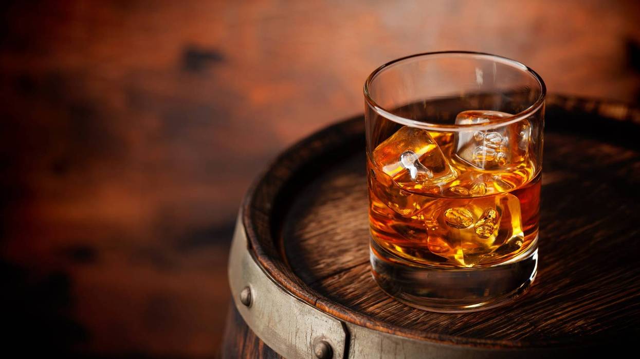 Glass of whiskey with ice cubes on the old barrel
