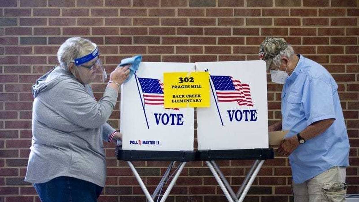 Glenda Patsel, left, wipes down a voting booth as Bobby J. Lambert fills out his ballot for the senate Republican candidates primary election, Tuesday, June 23, 2020, at Hidden Valley Middle School in Roanoke, Va.