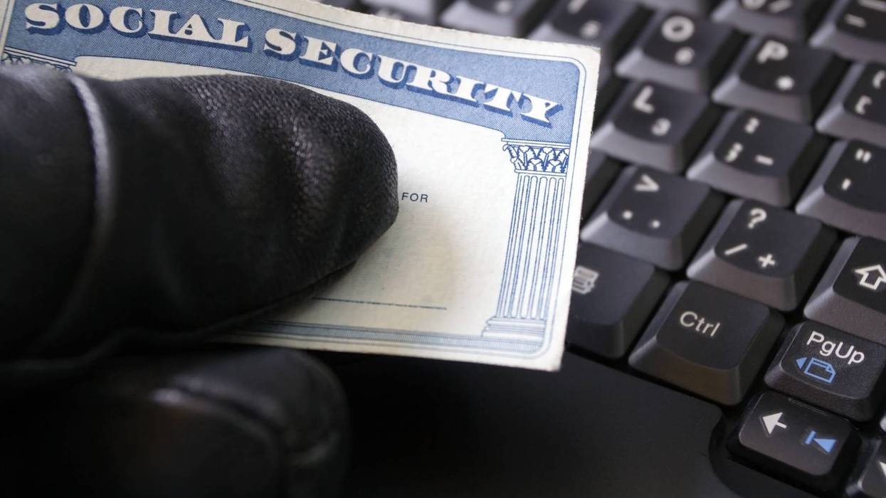 gloved hand holding a social security card in front of a computer keyboard