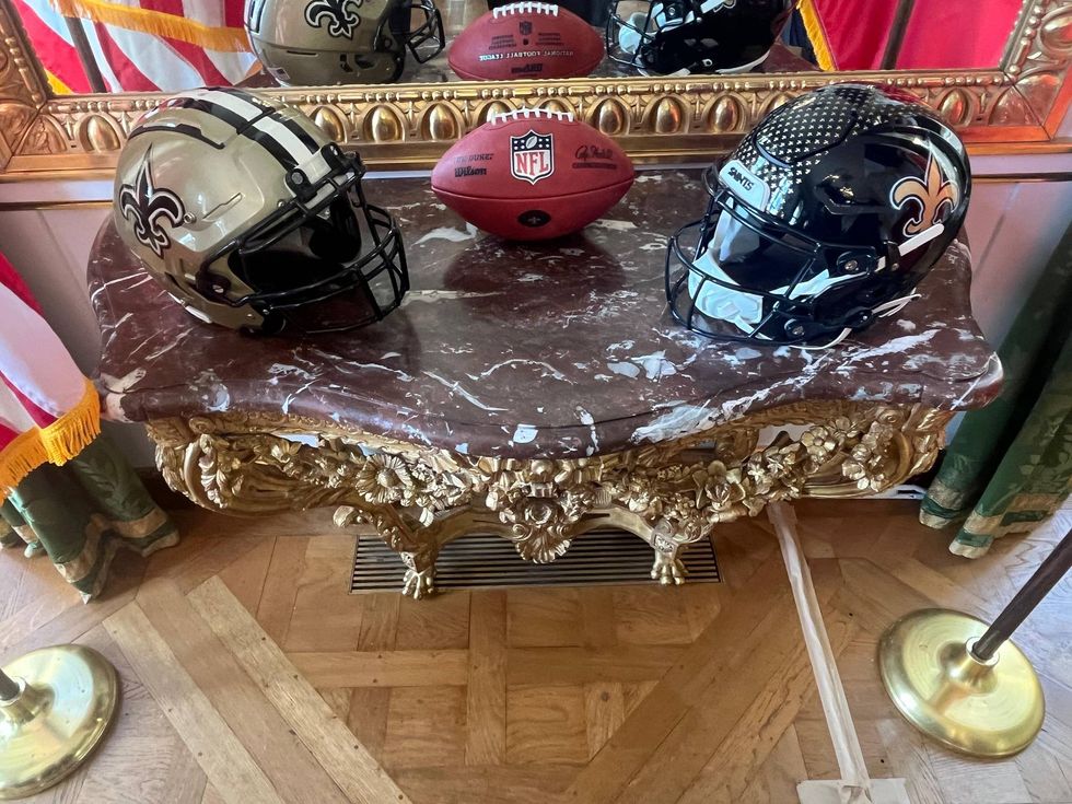 Gold and black New Orleans Saints helmets and NFL football on an ornate marble table.