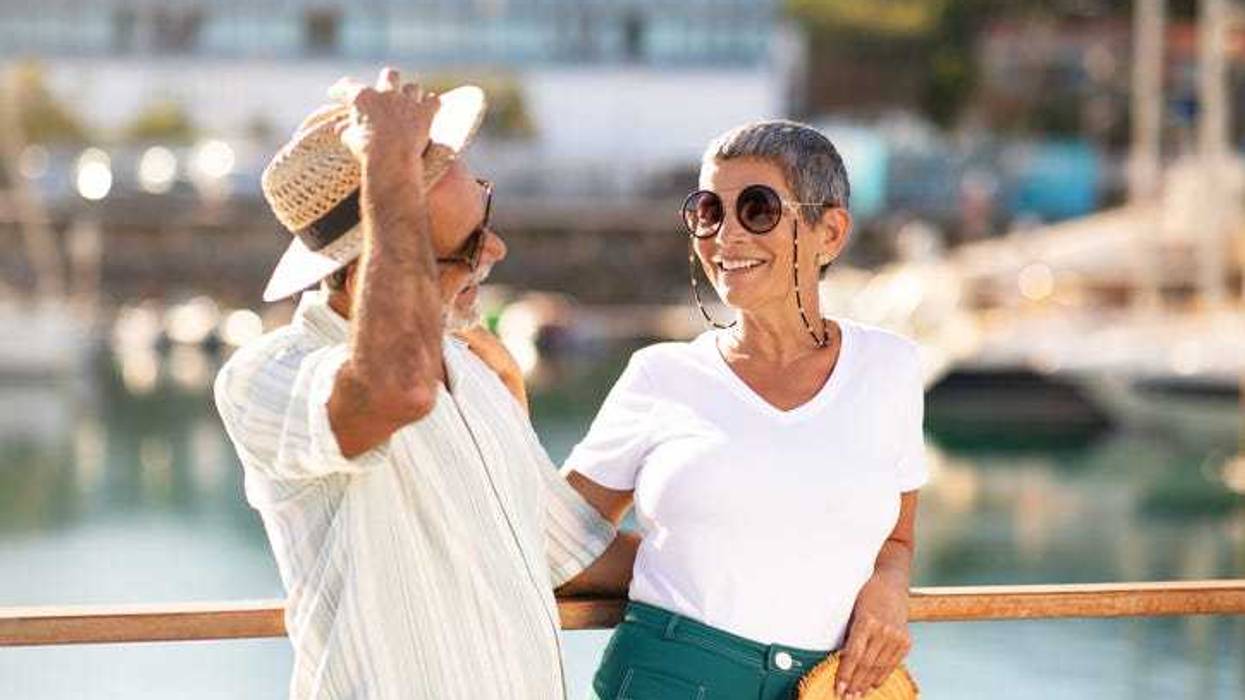 Golden Summer. Joyful Senior Man Holding Straw Hat And Hugging Wife, Posing Together At Marina Pier With Yachts And Luxury Sailboats, Laughing And Flirting Enjoying Sunny Day On Vacation Outdoor