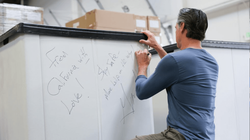 Governor Newsom packs emergency medical supplies for shipment to Ukraine, signing one of the bins on March 15, 2022 with a message reading "From California with love!"