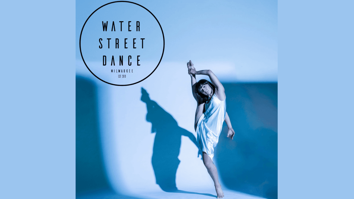 Graceful dancer in white slip dress with high leg extension & shadow on blue background. Water Street Dance.