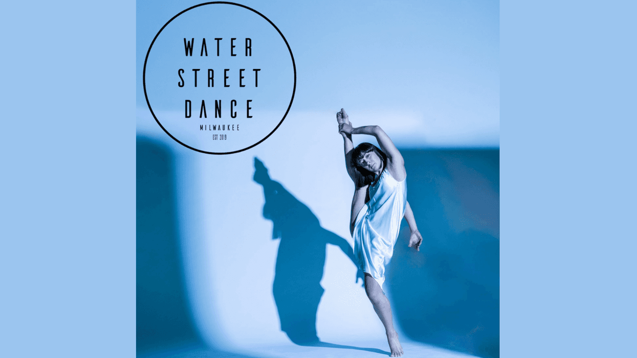 Graceful dancer in white slip dress with high leg extension & shadow on blue background. Water Street Dance.