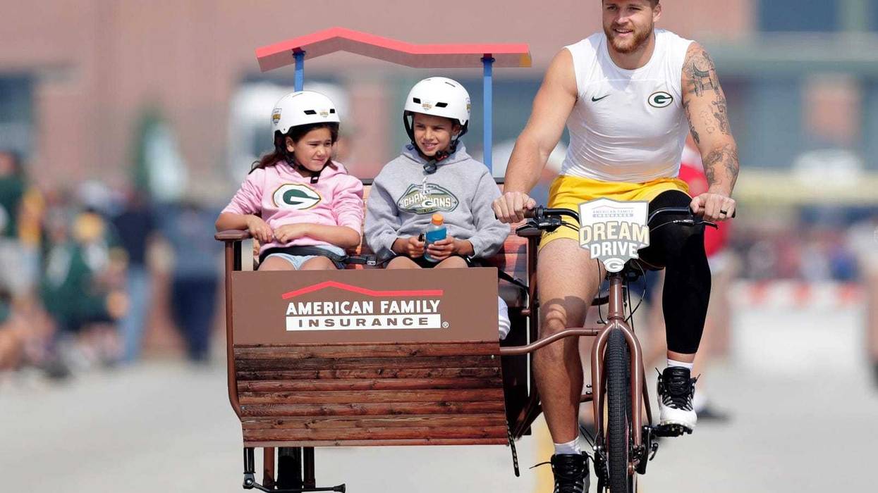 Green Bay Packers tight end Tucker Kraft (85) wears a cheesehead while participating in the Dream Drive bicycle ride before the start of practice on July 31, 2025, in Ashwaubenon, Wis.