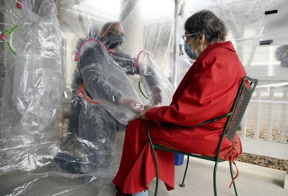 Gregg MacDonald holds hands with his 84-year-old mother, Chloe MacDonald, at a "hug tent" set up outside the Juniper Village assisted living center in Louisville, Colo., Wednesday, Feb. 3, 2021. The tent includes a construction-grade plastic barrier with built-in plastic sleeves to prevent the spread of the coronavirus.